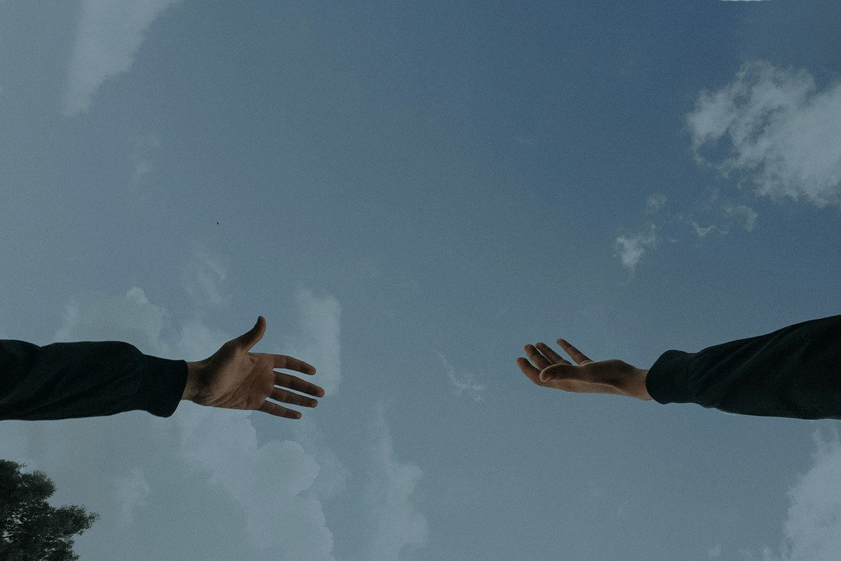 Two people reaching their hands toward one another against an open sky